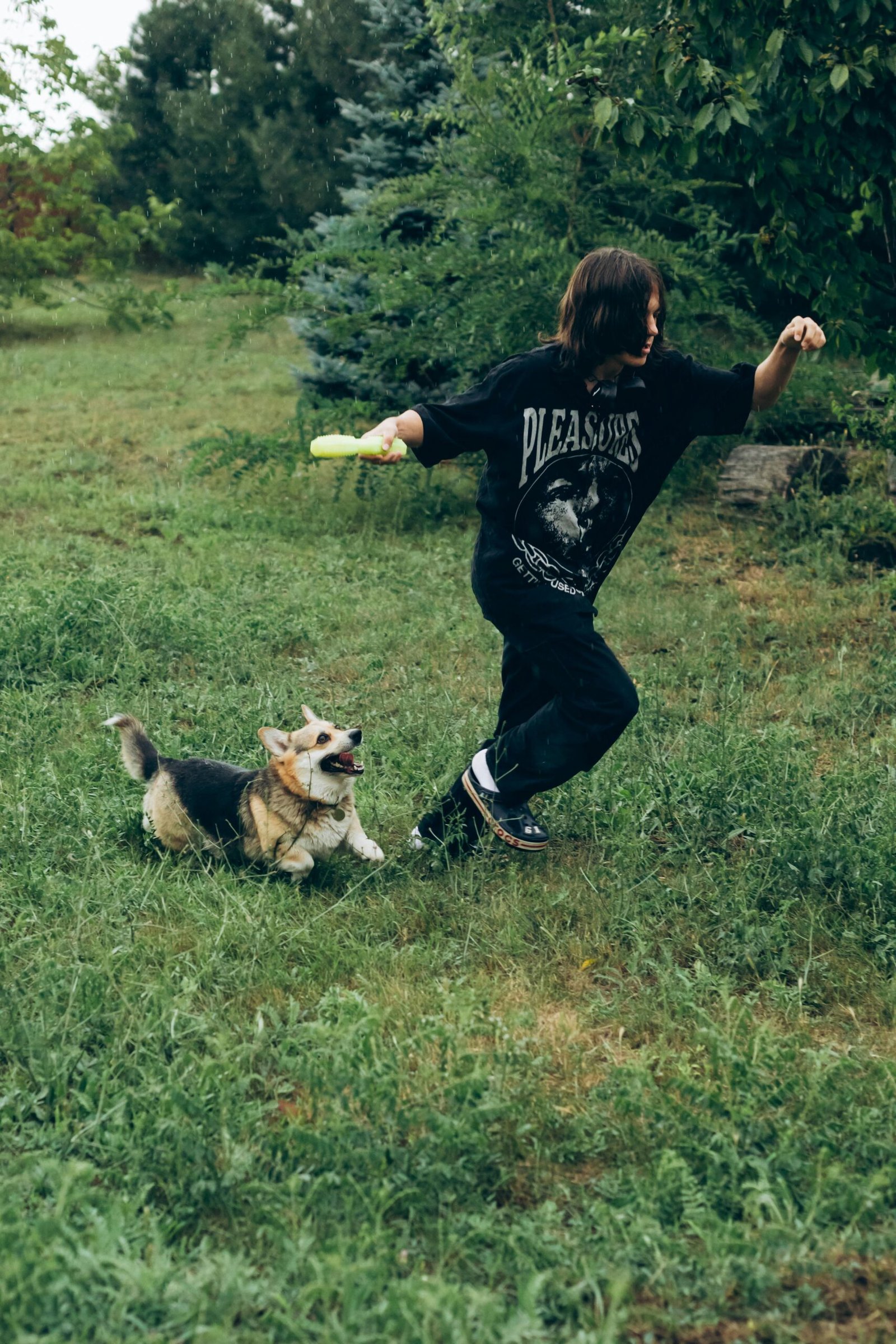 A teenager plays with a happy corgi in a lush green yard, capturing the joy of pet and owner bonding outdoors.